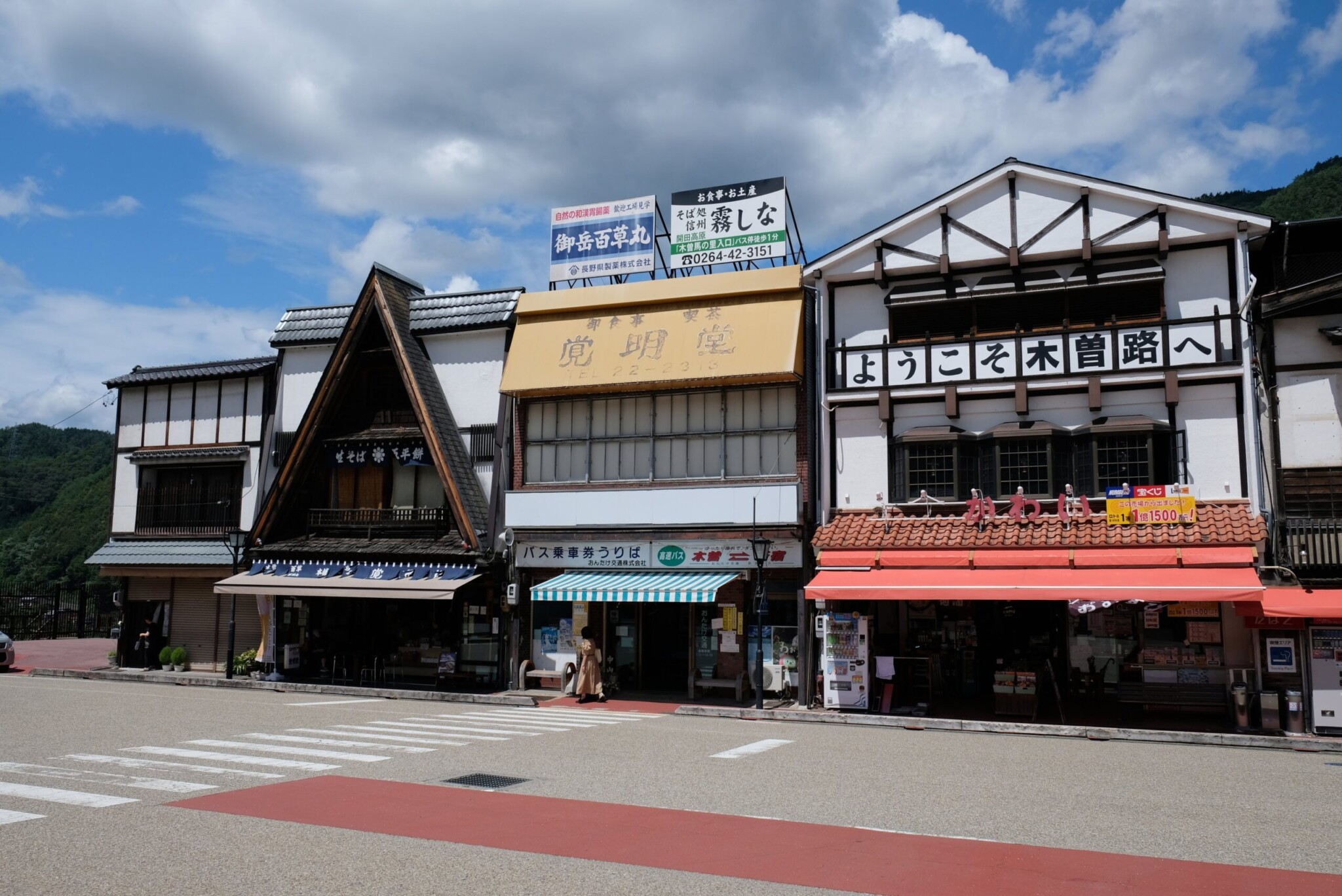 駅のプラットホームに停車中の特急列車の車両側面。車両は黒とダークグレーを基調とし、下部にオレンジ色と白のラインが走っている。窓ガラスには車内の座席(白いヘッドカバー付き)や、乗客(マスクや帽子を着用した人物)の姿が映っている。ホームの天井や柱、黄色い点字ブロックも写り込んでいる。