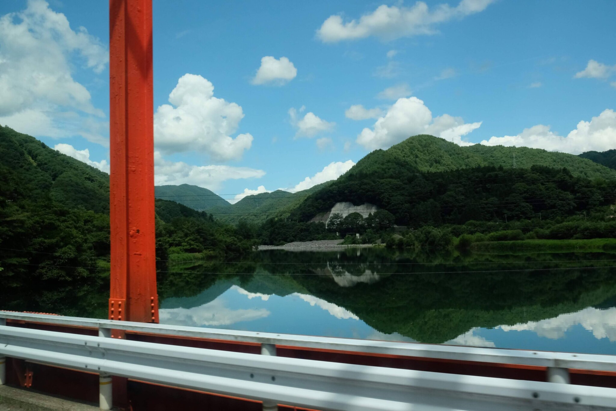 走行中または停車中のバスの車内から前方を撮影した風景。車内には緑色の幾何学模様のシートが並び、白いヘッドカバーがかけられている。手すりや柱は鮮やかな黄色。窓の外には山が迫る景色や建物(「ようこそ」の文字が一部見える)が写っている。車内は比較的空いている。