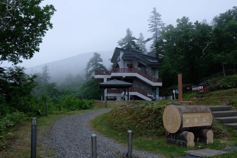斜里岳の登山拠点である山小屋「清岳荘」。霧に包まれた山肌を背に建つ石造りと木造の建物。