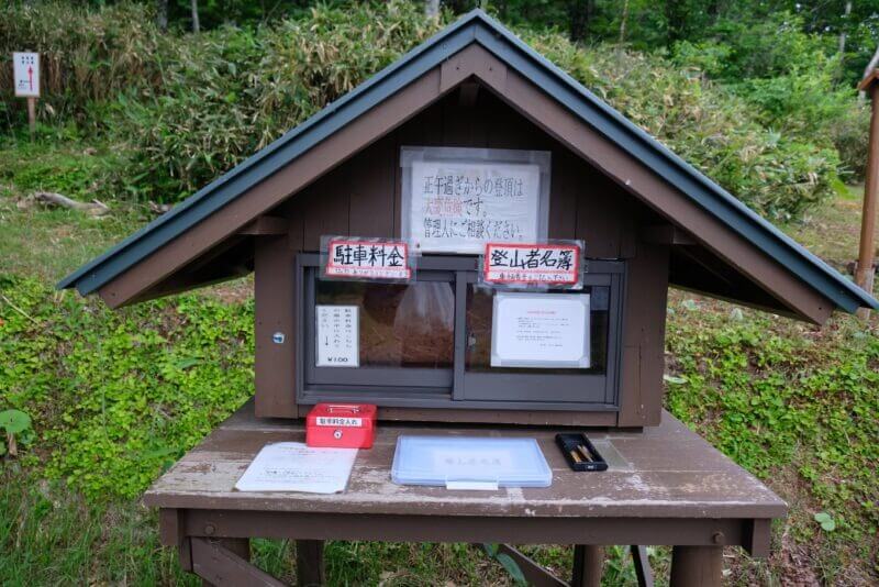 斜里岳登山口に設置された登山者名簿と駐車料金箱。木造の小さな小屋の形をしている。