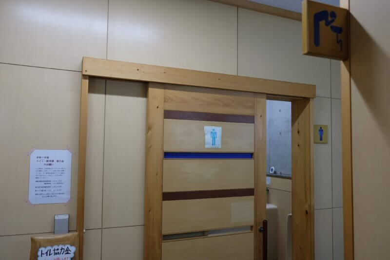 トイレの木の引き戸と、協力金のお願いが書かれた案内掲示。
