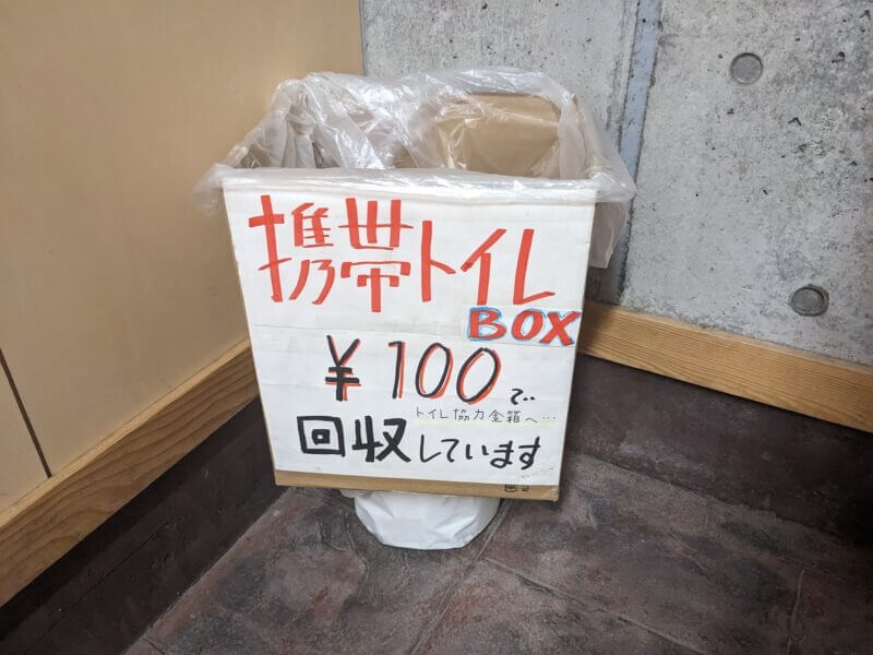「携帯トイレBOX」と書かれた回収用の段ボール箱。回収費100円の案内。