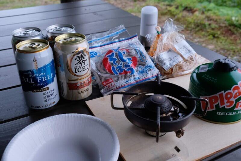 テーブルに並べられた夕食の食材。ノンアルビール、袋蕎麦、バーナーなど。