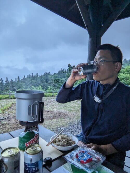 霧の中で夕食を食べ、ノンアルビールを飲む男性。背景は真っ白な霧。