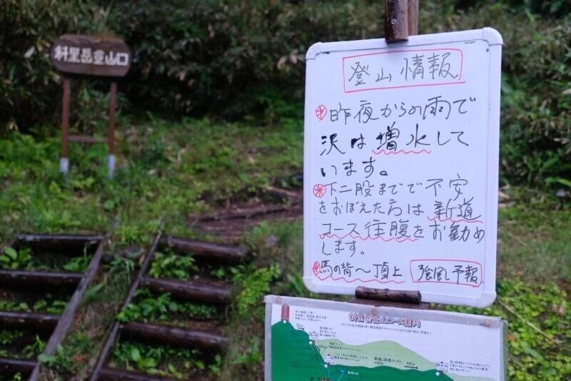 登山口のホワイトボード。雨による沢の増水と、馬の背付近の強風への注意喚起が書かれている。
