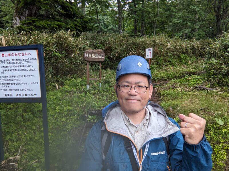 ヘルメットとレインウェアを装備し、登山口の前でポーズをとるブログ主。