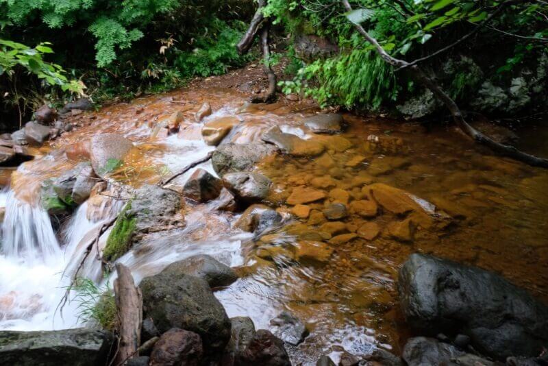 段差を流れ落ちる沢の水と、苔の生えた岩. 水流が白い糸のように見える。