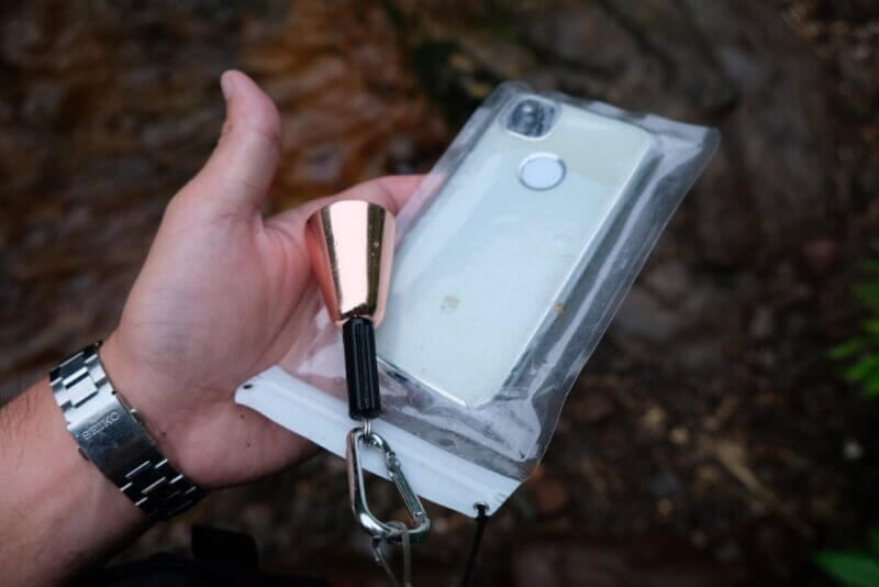 防水ケースに入れたスマホとピンクゴールドのクマ鈴を持つ手元のアップ。
