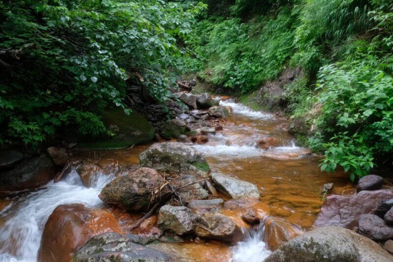 霧に包まれた沢の遠景。赤茶けた岩が点々と続き、奥へと消えている。