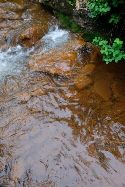 透明な水が流れる川底の赤茶けた岩のクローズアップ。