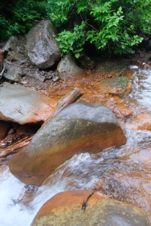 水の流れに洗われる、表面が滑らかで巨大な赤茶色の岩のアップ。