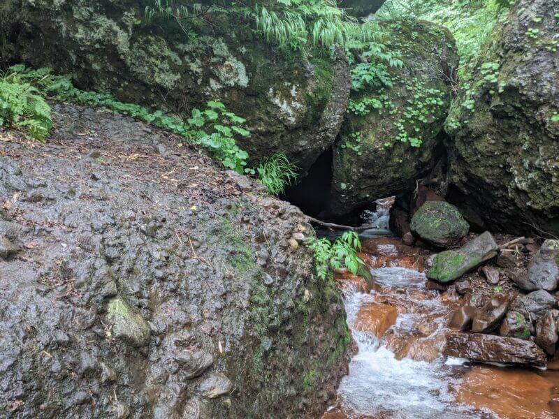 折り重なる大きな岩の下を潜るように流れる沢水
