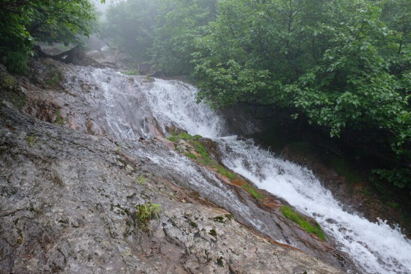 階段状の岩場を水が流れ落ちる小規模な滝。岩の一部には緑の苔が付着している。