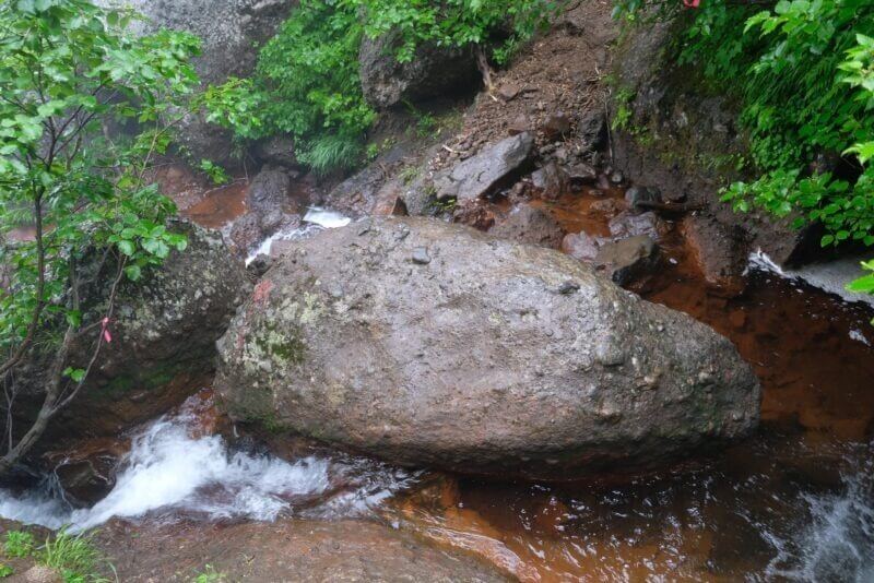 沢の中に置かれた、存在感のある巨大な丸い転石。周囲の水は赤褐色。