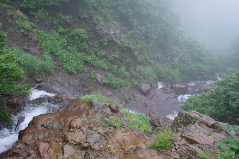 滝の落ち口から霧の底へ向かって流れる水を見下ろした視点