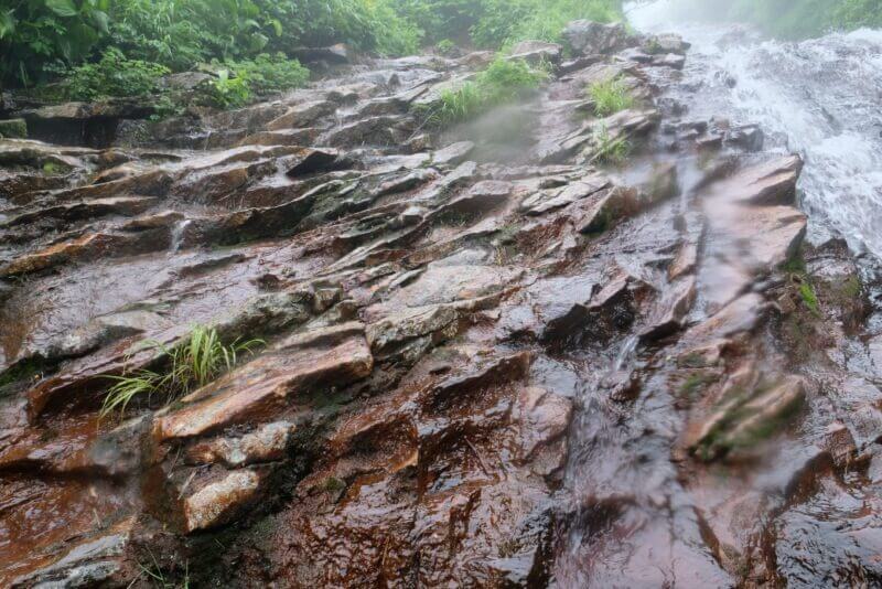 板状の岩が重なる地形を勢いよく流れる雨水のクローズアップ