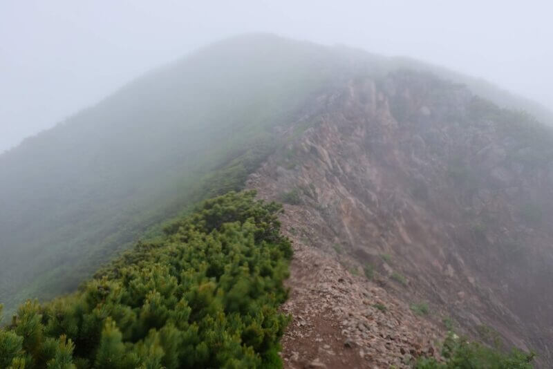 霧に包まれた急峻で切り立った痩せ尾根の登山道