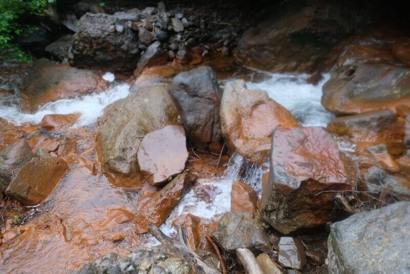 酸化鉄で赤茶色に染まった岩の間を流れる白い飛沫の沢水。
