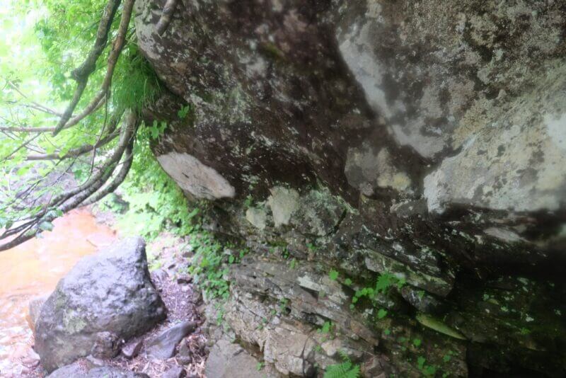 巨大な岩のオーバーハングと、その下を通る沢沿いの登山道。