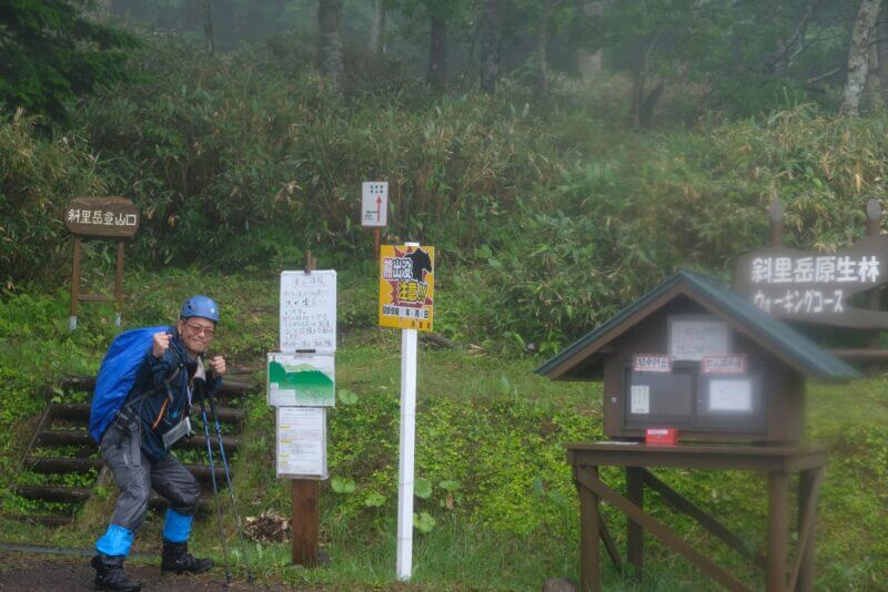 斜里岳登山口の看板前でポーズをとる登山姿の男性
