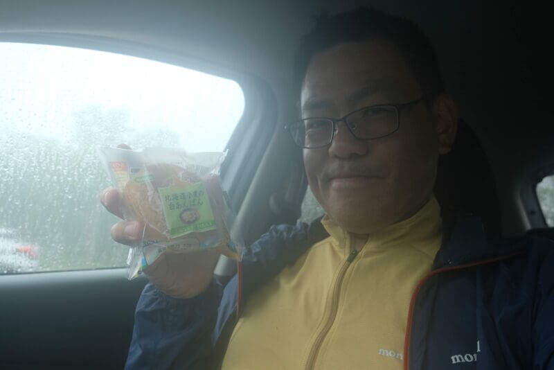 車内で菓子パンを持つ眼鏡の男性
