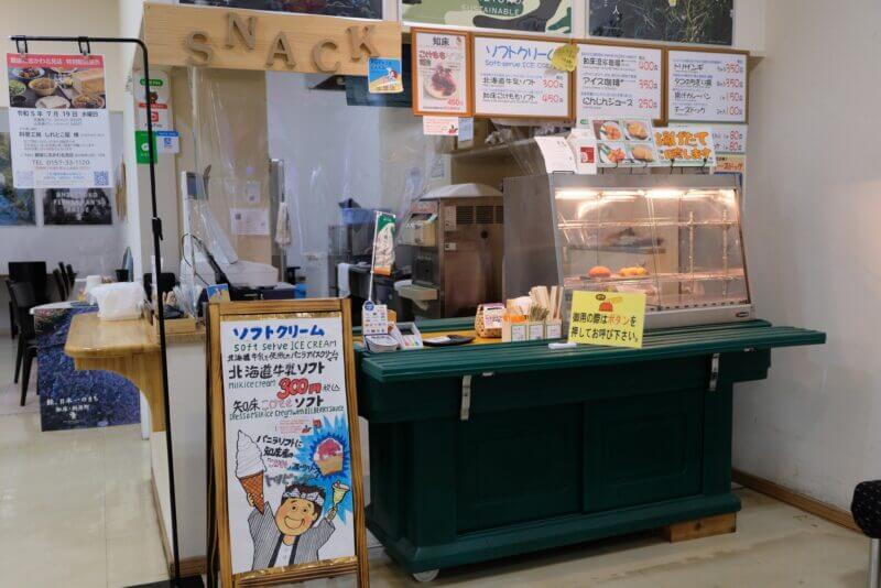 知床の売店のスナックコーナー。ソフトクリームや鹿肉カレーパンなどのメニュー看板と揚げ物の什器が見える。