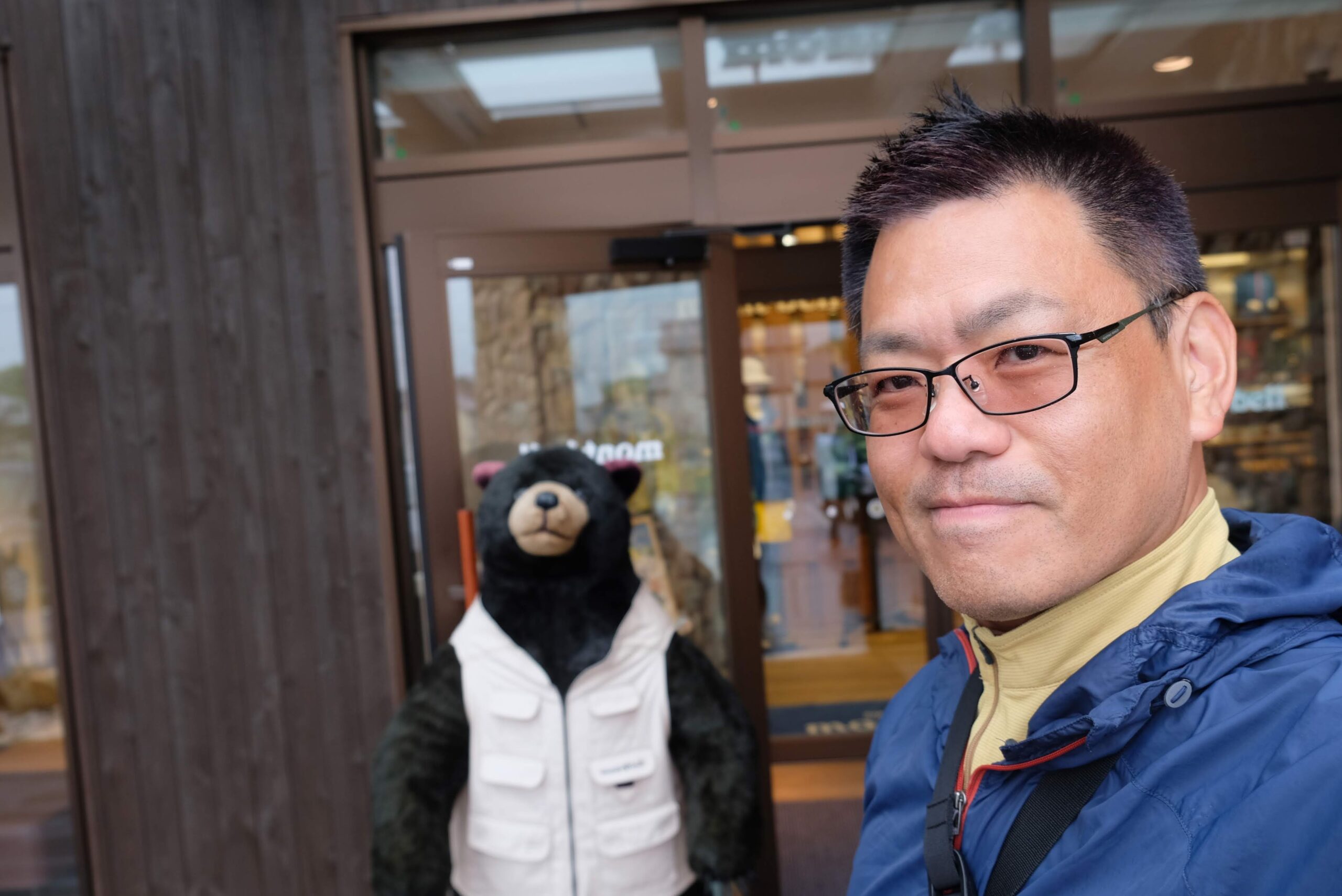 モンベルの店舗前で、モンベルベアのぬいぐるみと共に自撮りをするブログ主。