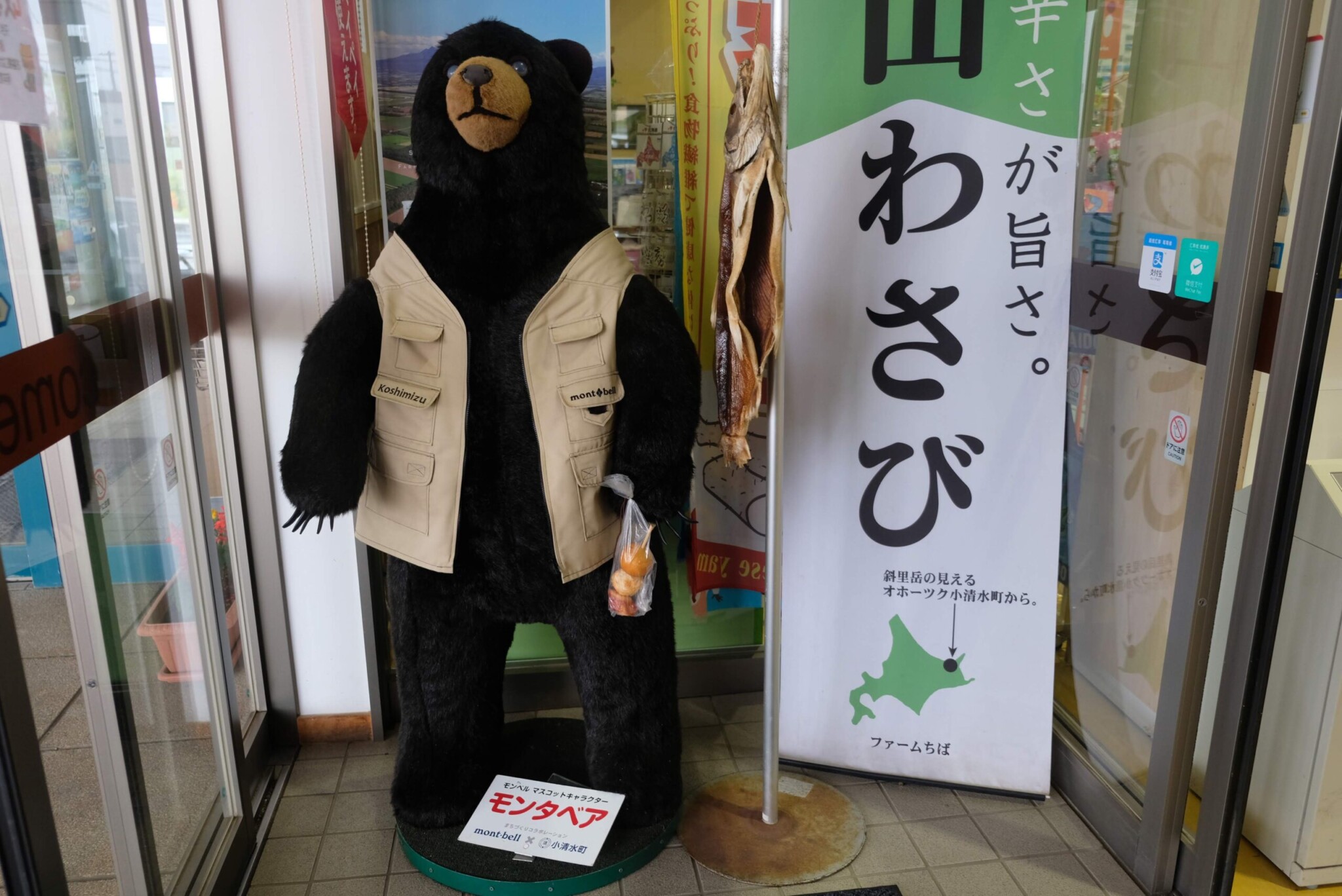 小清水町の道の駅に立つモンベルのマスコット、モンタベアのぬいぐるみ。フィッシングベストを着用し、ジャガイモの袋を提げている。