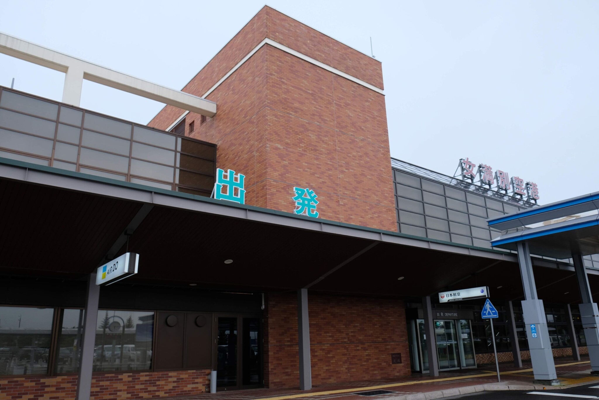 夕暮れ時の女満別空港ターミナルビル。レンガ調の壁面に「出発」の文字。