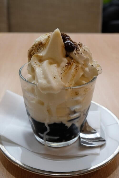 ガラス容器に盛られたコーヒーゼリーパフェ。ソフトクリームの上にコーヒー豆と粉末がトッピングされている。