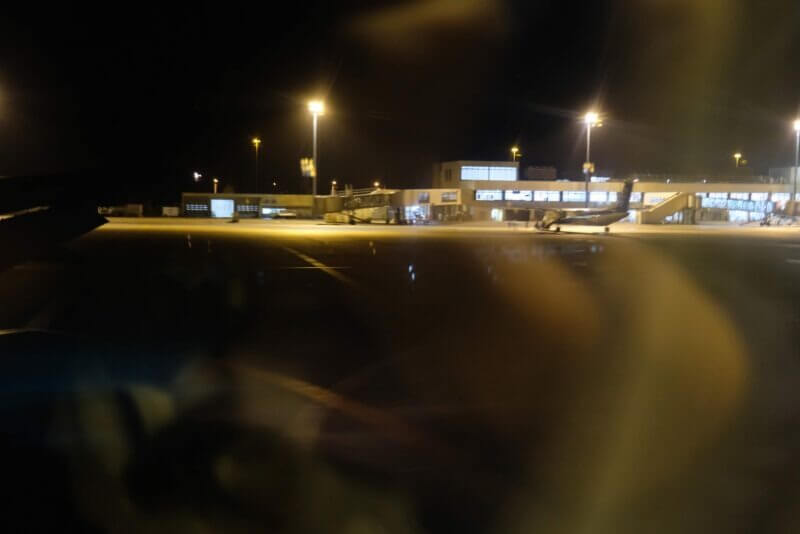 夜 of 空港、誘導灯に照らされた駐機場の風景。暗闇の中に機体のシルエットが見える。