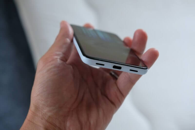 液晶画面に青い縦線のノイズが入ったスマートフォンの底面とUSBポートを持つ様子