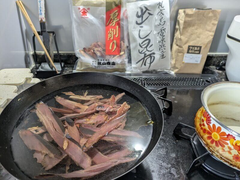中華鍋で厚削り節と昆布から出汁を取る様子。背景には秋山商店の節と利尻昆布の袋。