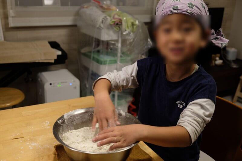 バンダナを巻いた子供がボウルの中でそば粉と水を混ぜる水回しの工程。