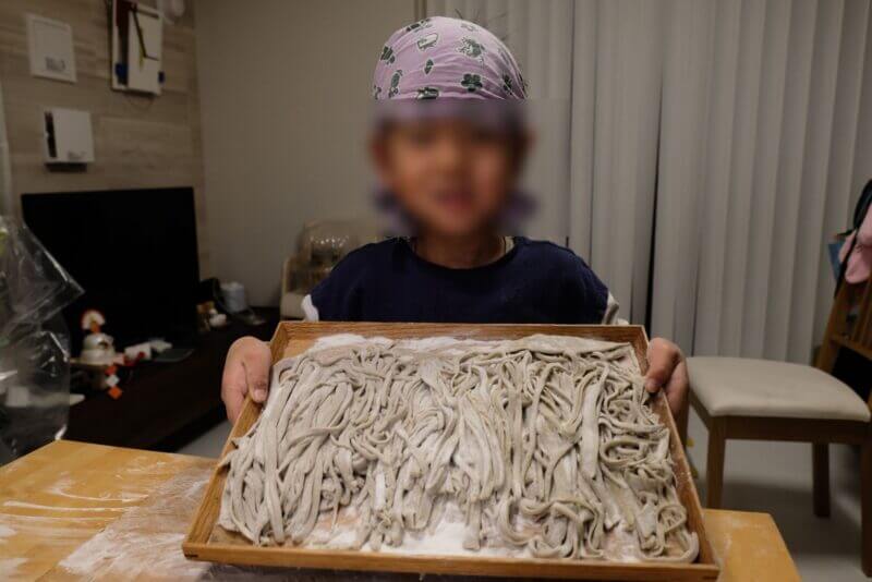 切り終えた不揃いなそばを木製の盆に載せて披露する子供。