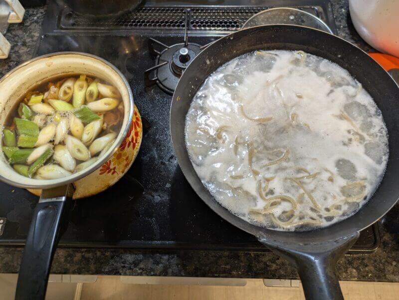 コンロの上で肉南蛮のつゆを煮込み、隣の中華鍋でそばを茹でる様子。